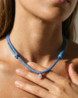 Close-up of a model wearing a blue paracord necklace with a hand touching her shoulder.