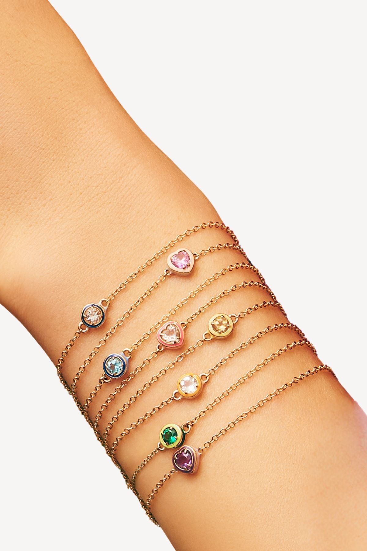 Model wearing multiple chain bracelets with semi precious stones in round brilliant cut and heart cut