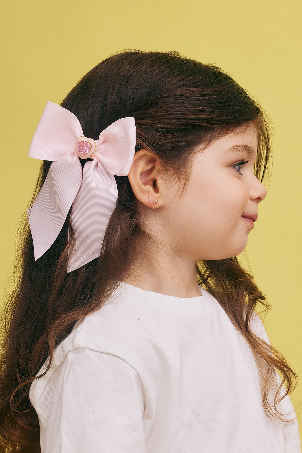 Young girl wearing pink hair bow clipped into dark hair against yellow background