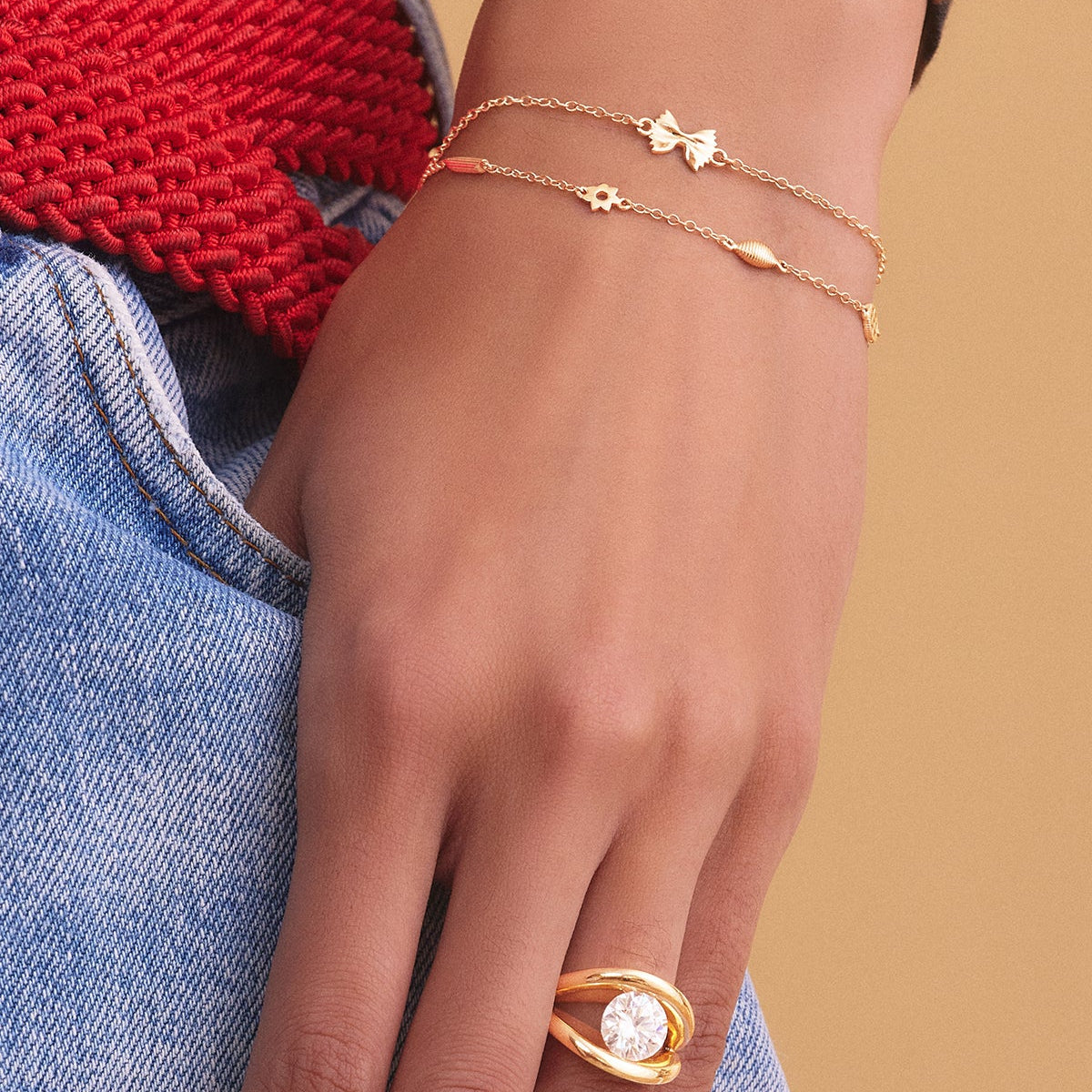 Model wearing bowtie shaped charm gold chain bracelet with another gold chain bracelet and yellow gold and diamond ring