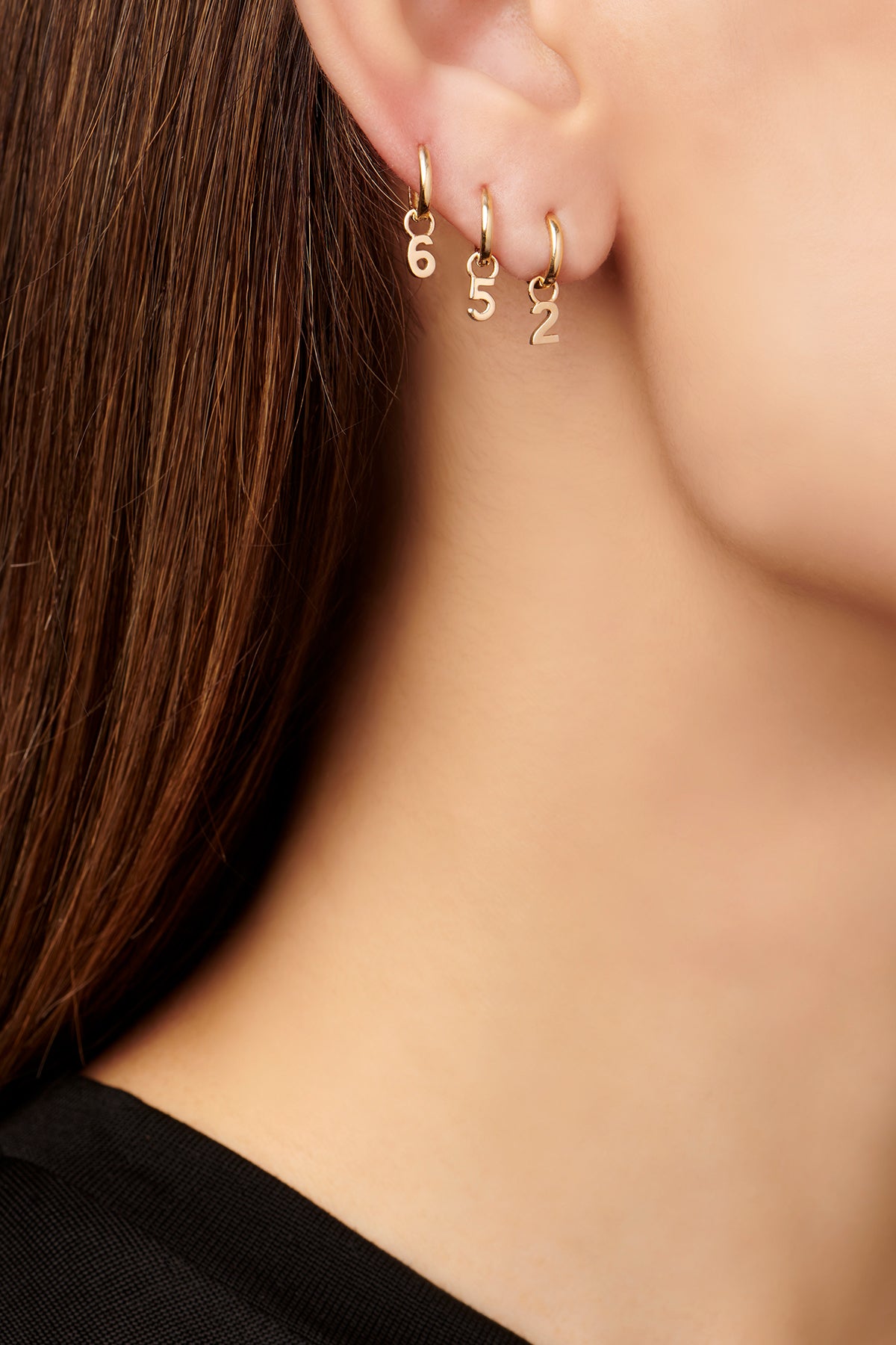 Model wearing three different gold hoop earrings with a number "6', "5" and "2"