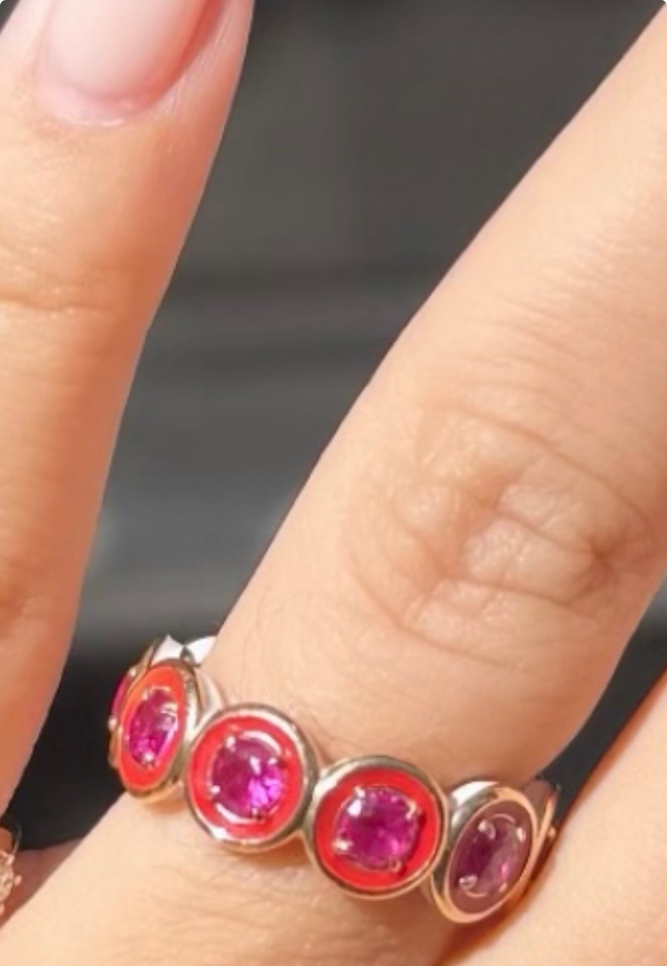 Close-up of a ring with pink gemstones on a finger against a dark background