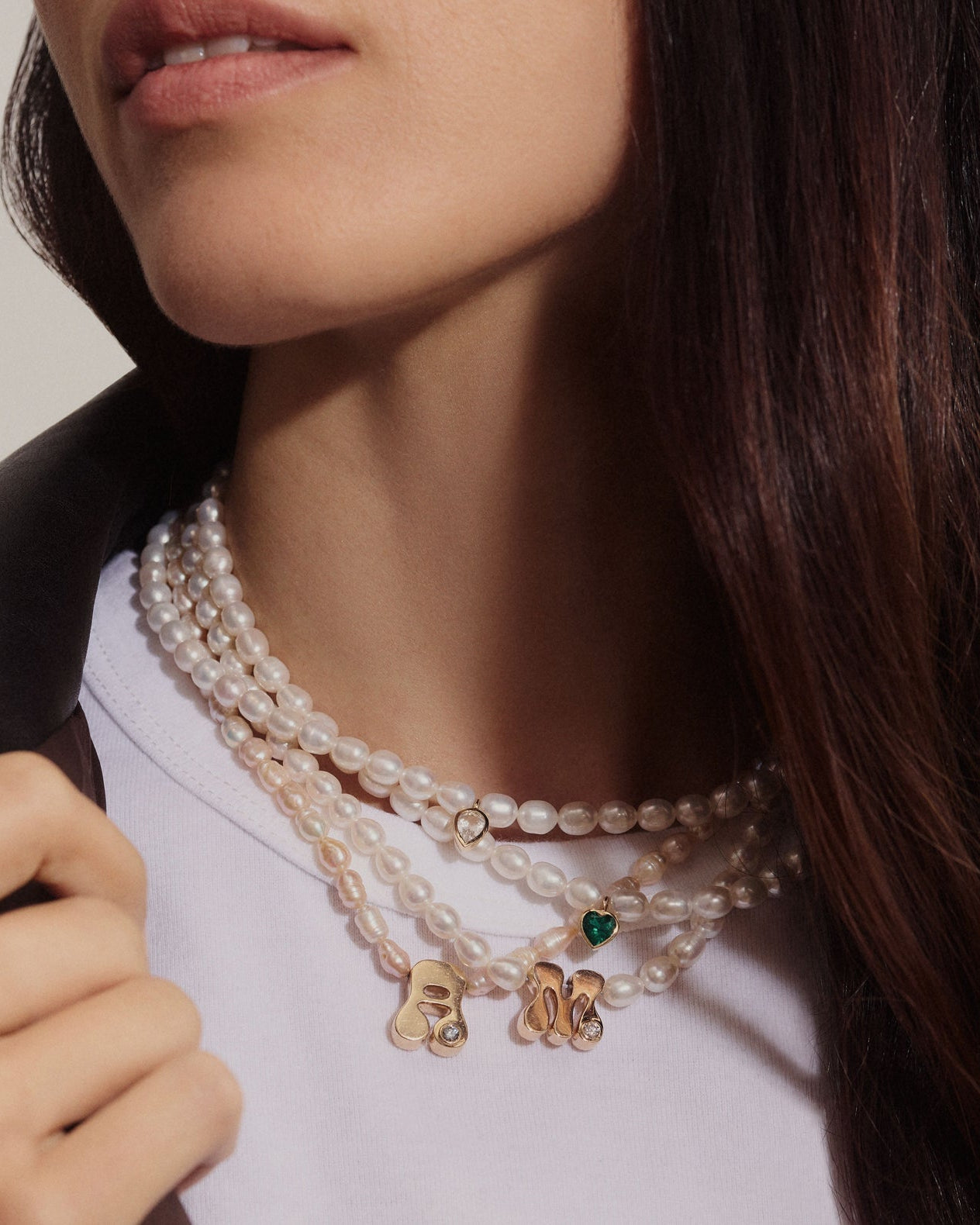 Close-up of a model wearing a multi-strand pearl necklace with gold charms and a small green heart accent.
