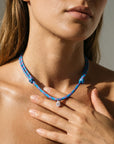 Close-up of a model wearing a blue paracord necklace with a hand touching her shoulder.