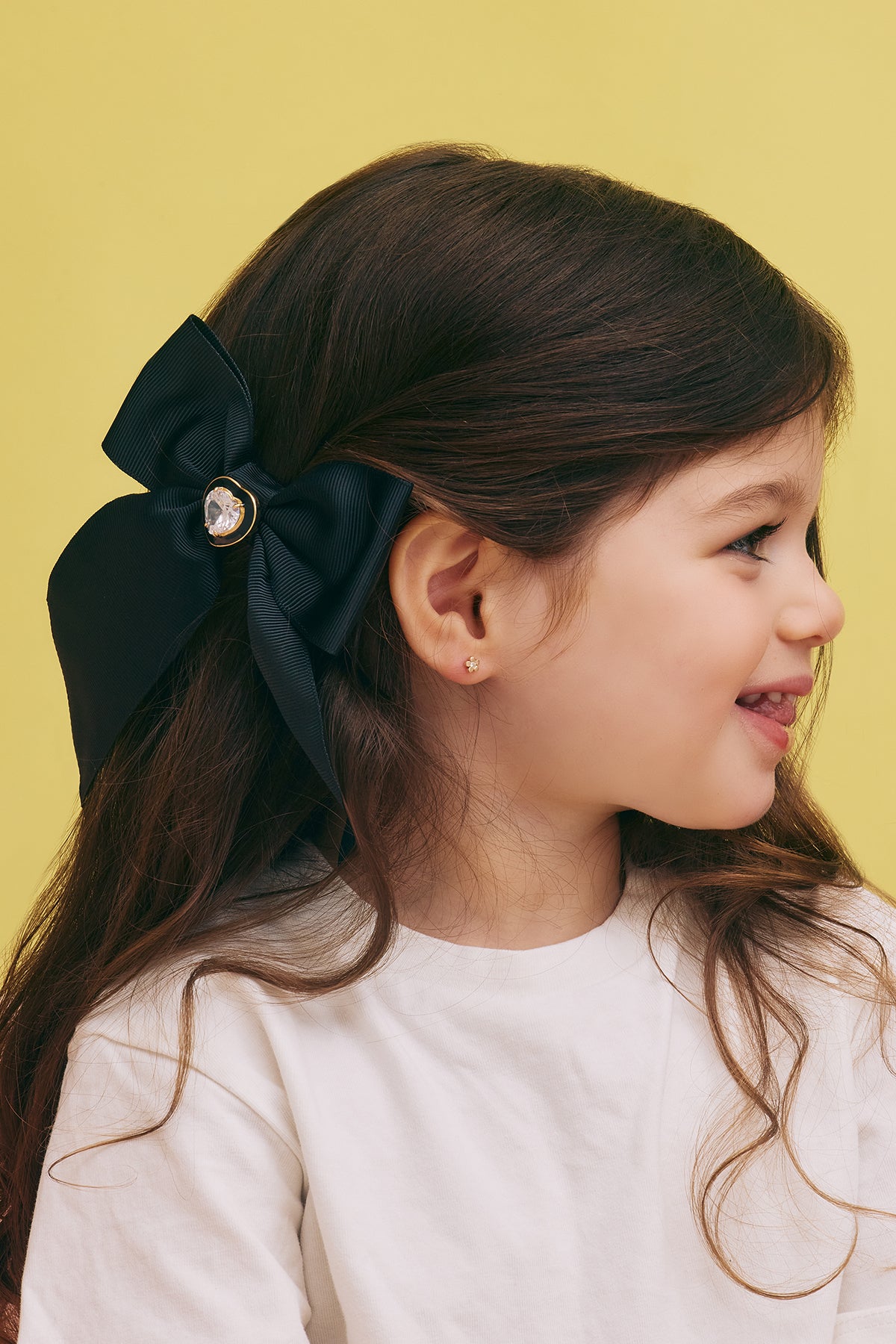 Young girl with a large black bow in her hair against a yellow background