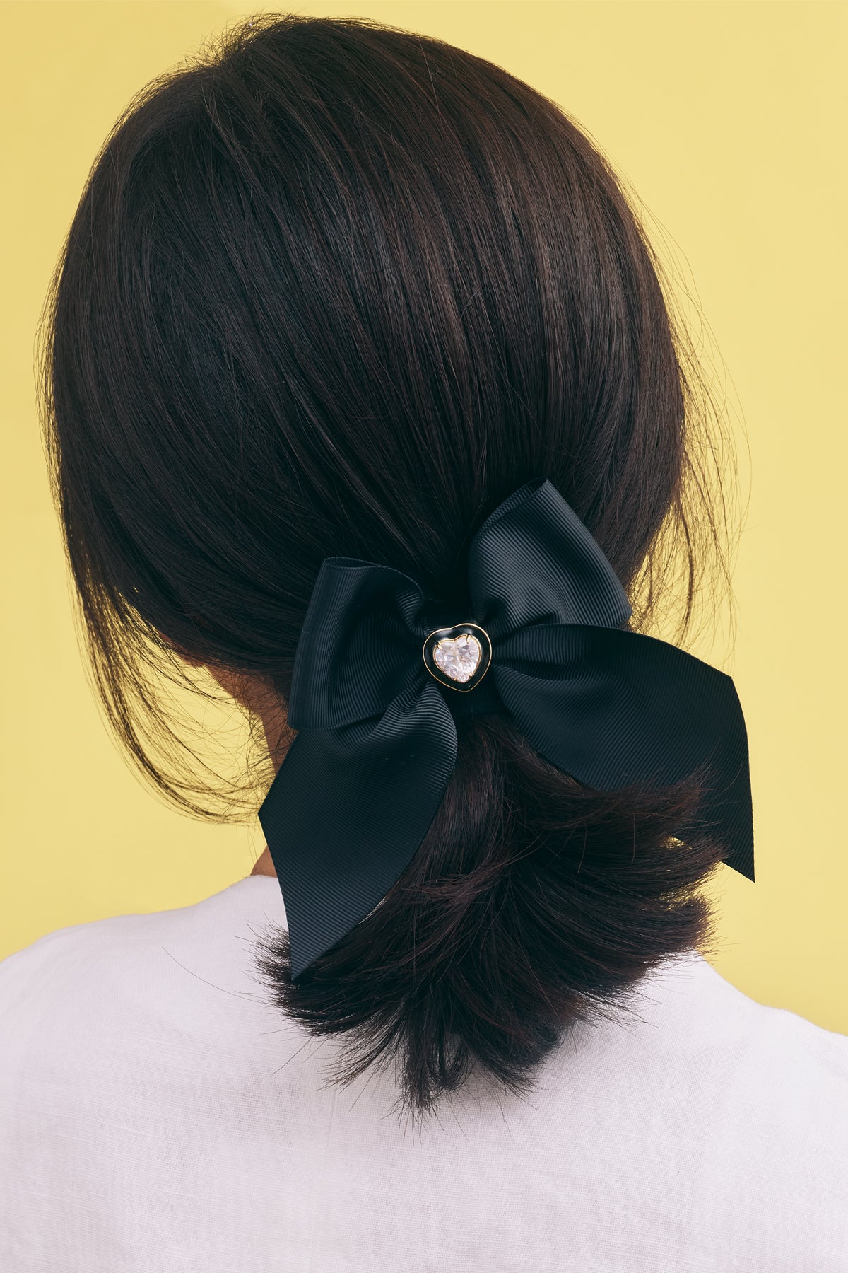 Black hair bow with a heart-shaped center on a yellow background