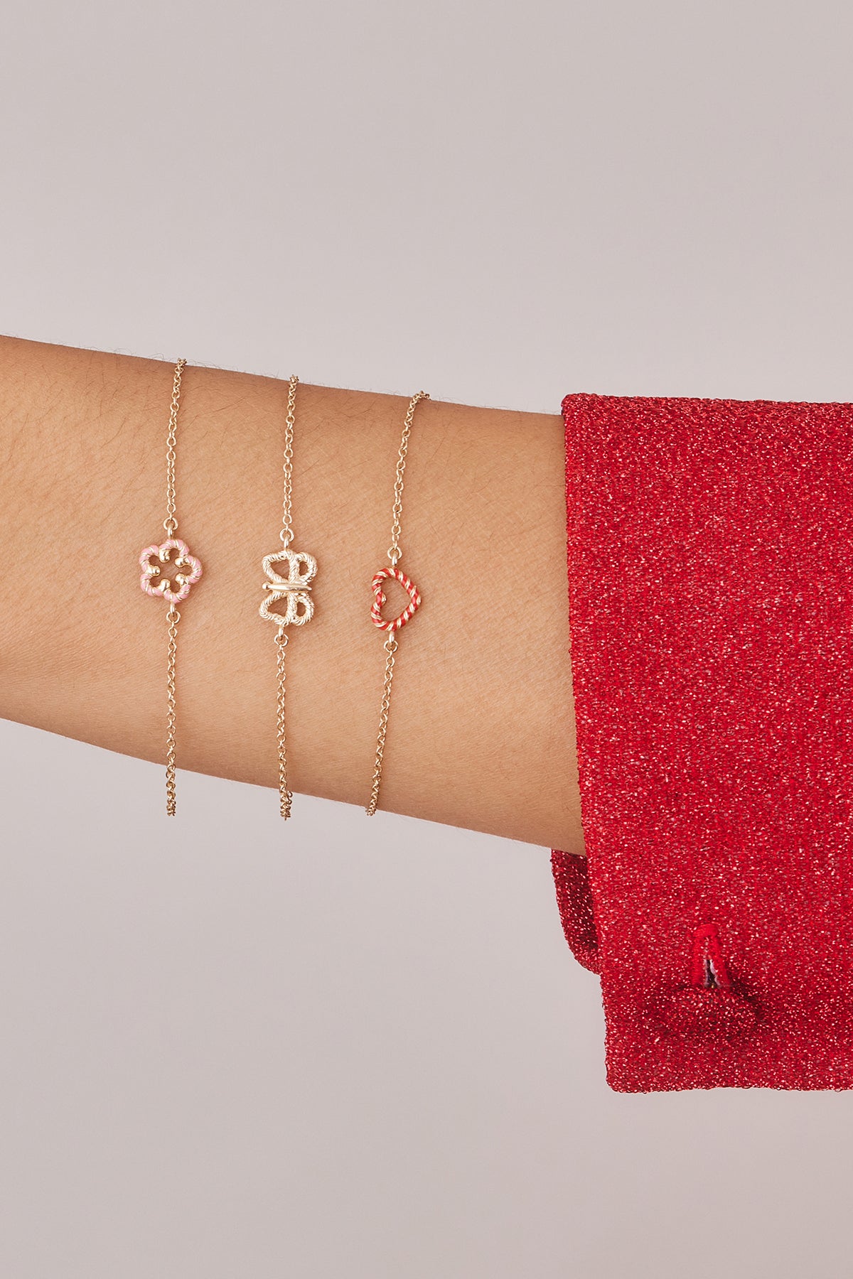 Model stacking bracelets with a floral motif, a butterfly motif, and heart motif on wrist.