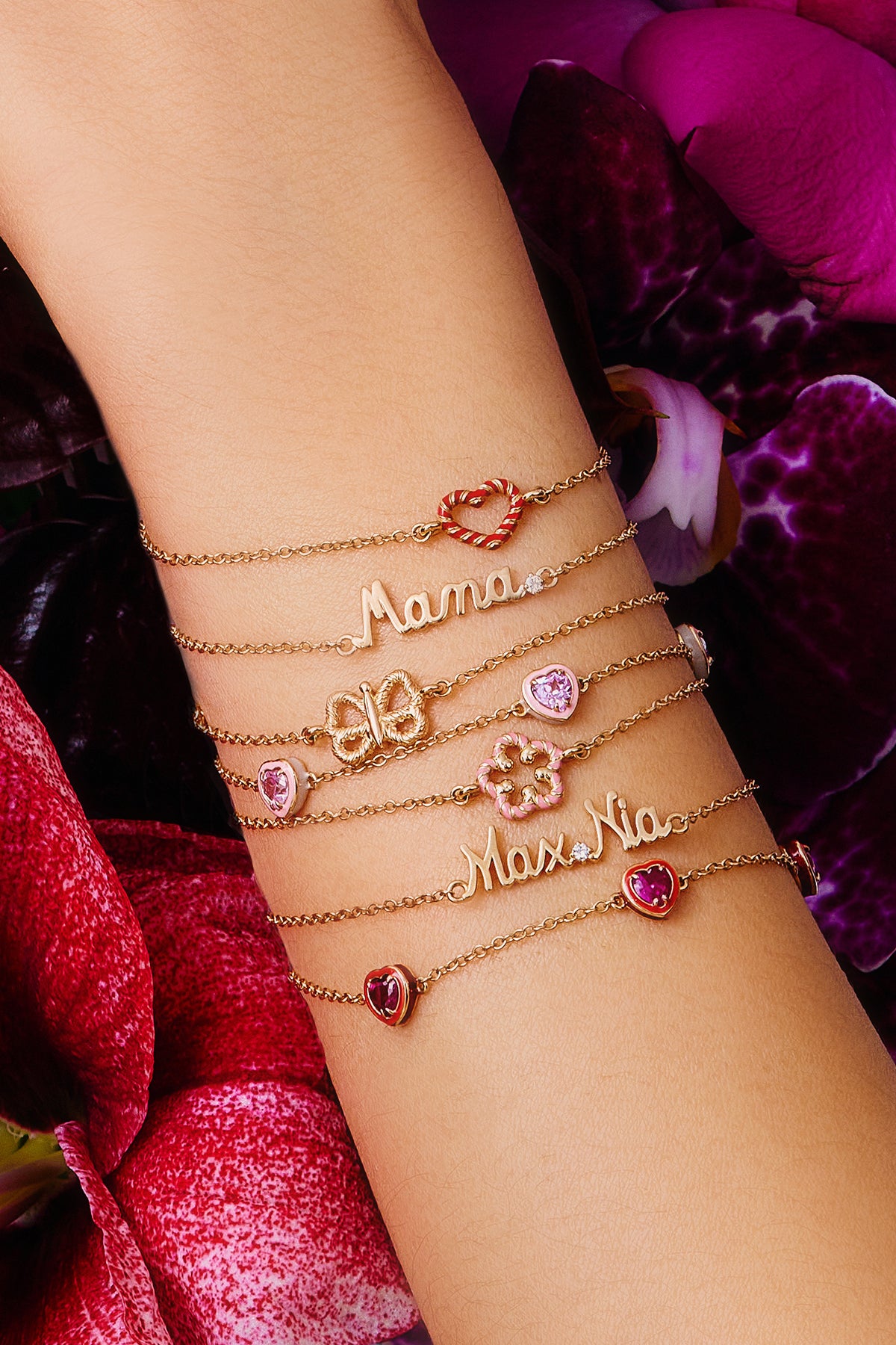 Model stacking multiple bracelets with a floral motif, a butterfly motif, and heart motif and few with "Mama," and "Max.Nia."